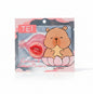 A hand holds a package of TEI Cartoon & Collagen Plumping Lip Mask against a background of green foliage. The packaging features a cute cartoon capybara sitting in a pink lotus flower, with a pink lip mask visible through a clear window.